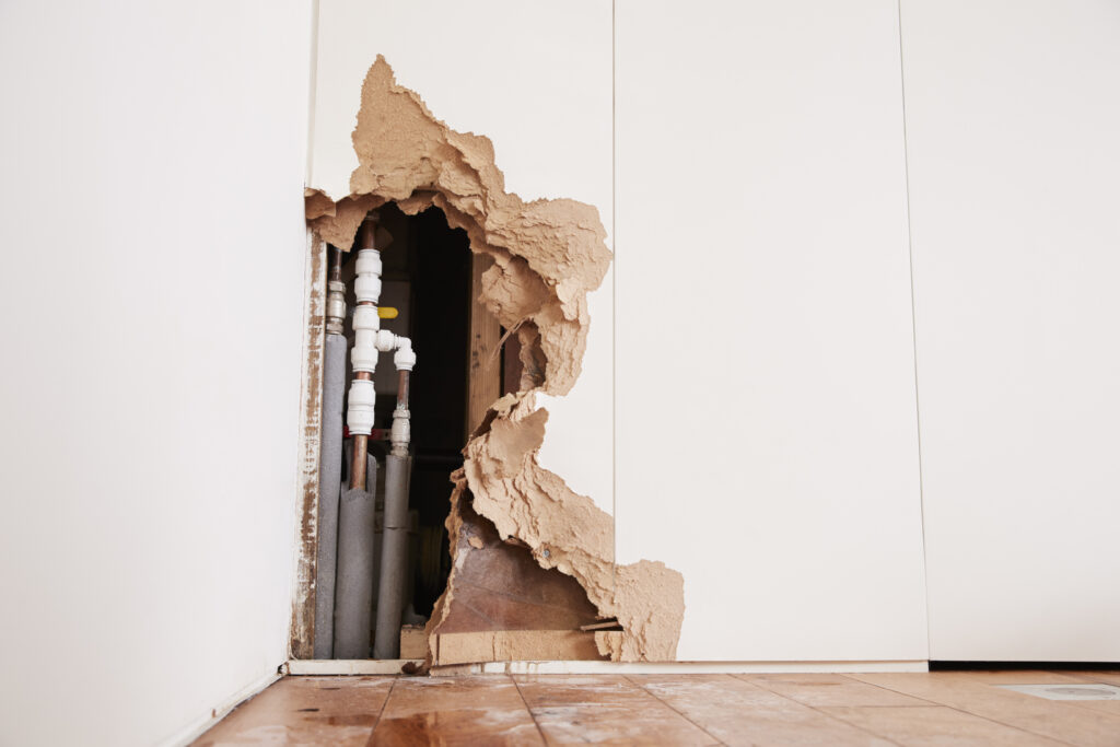 Damaged wall exposing burst water pipes after flood
